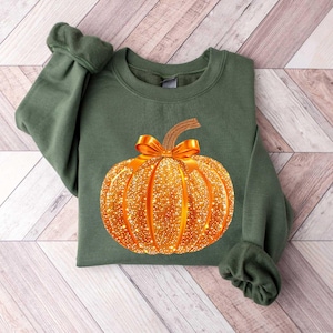 May include: A green sweatshirt with a gold glitter pumpkin design. The pumpkin has a brown stem and a gold bow.