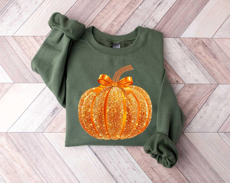May include: A green sweatshirt with a gold glitter pumpkin design. The pumpkin has a brown stem and a gold bow.