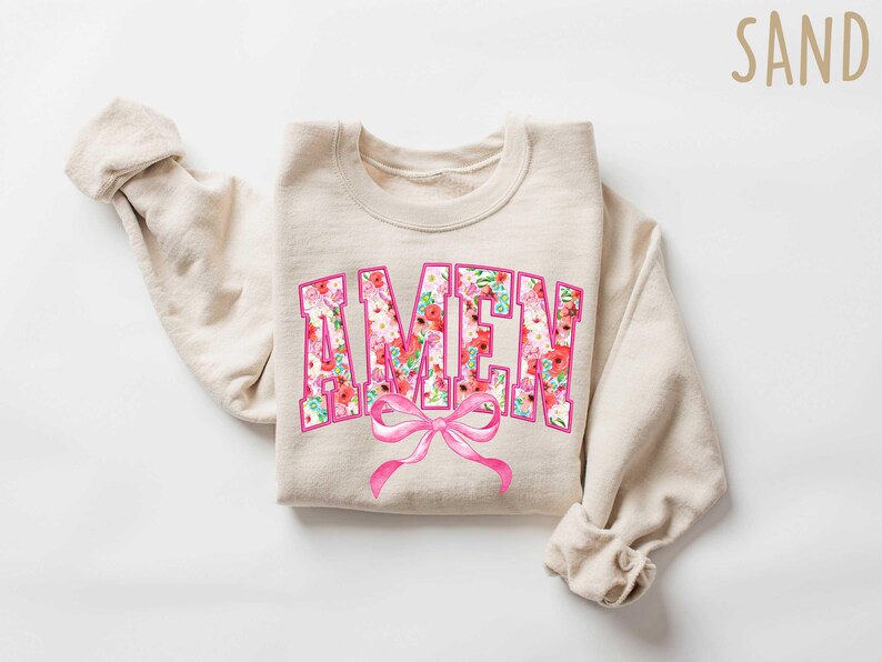 May include: A beige sweatshirt with a floral print "AMEN" graphic and a pink bow.