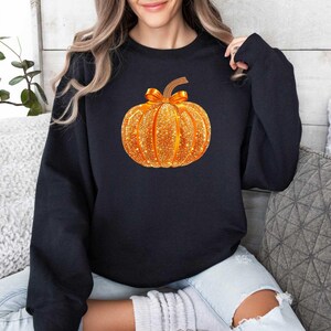 May include: A black sweatshirt with a sparkly gold pumpkin design. The pumpkin is a fall-themed design.