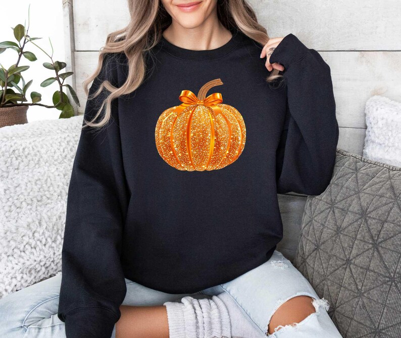 May include: A black sweatshirt with a sparkly gold pumpkin design. The pumpkin is a fall-themed design.