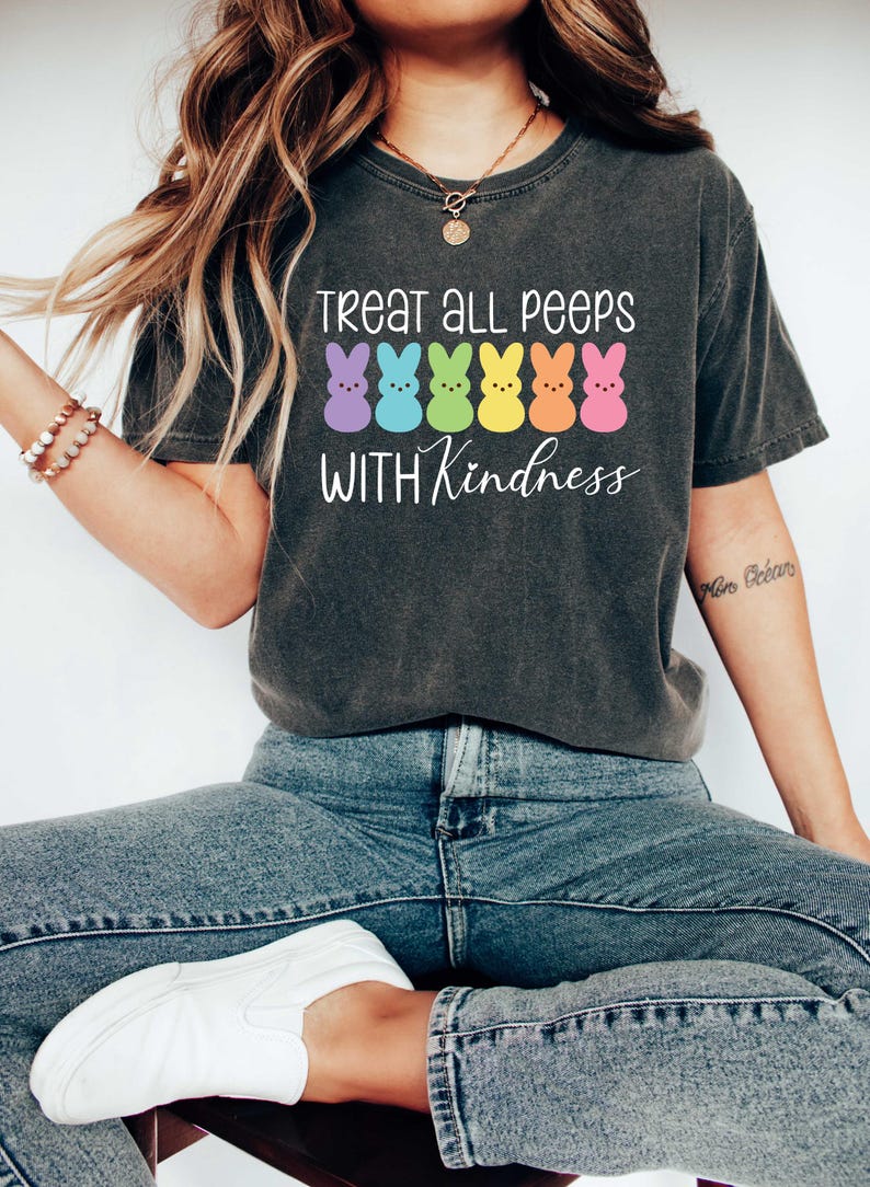 May include: A dark grey t-shirt with a white graphic that says "Treat all peeps with kindness". The graphic features a row of six colorful marshmallow peeps.