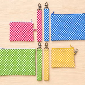 Peut inclure: Divers accessoires à carreaux vichy colorés, comprenant des pochettes zippées et des porte-clés. Les pochettes sont rouges, bleues, vertes et jaunes, tandis que les porte-clés assortis. Tous les articles ont des fermetures argentées.