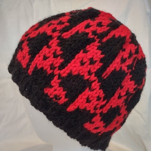Puede incluir: Un gorro de punto negro y rojo con un patrón de pata de gallo. El gorro está en una cabeza de maniquí blanca.