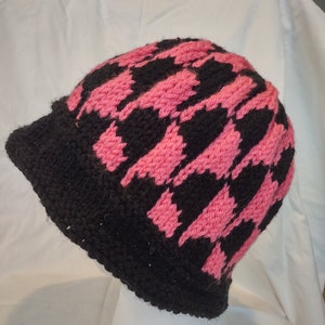 Puede incluir: Un gorro de punto negro y rosa con un patrón de pata de gallo.