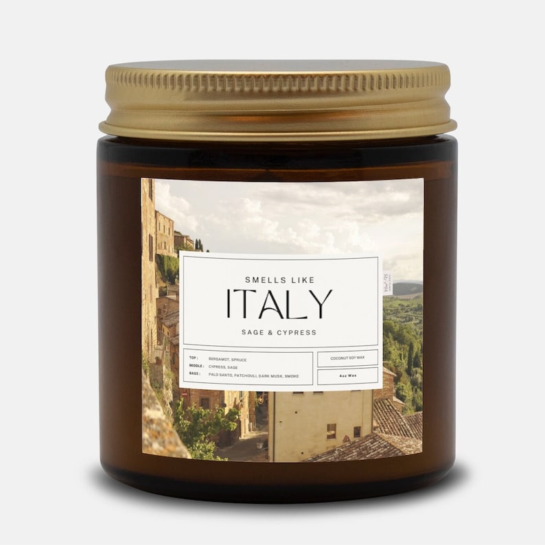 May include: A brown glass candle jar with a gold lid. The label features a photo of an Italian village and the text "Smells Like Italy Sage & Cypress". The candle is made with coconut soy wax.