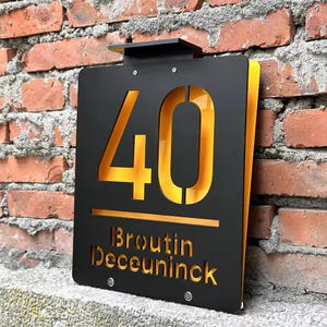 May include: Black metal house number sign with a gold 40 and the name "Broustin Deceuninck" in gold lettering.