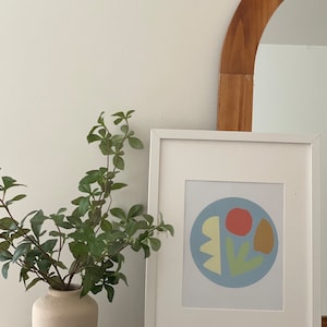 以下が含まれることがあります： 青い円の中に、黄色、緑、赤、茶色の抽象的な形が描かれた額装されたプリント。形は葉、花、幾何学的な形を連想させる。