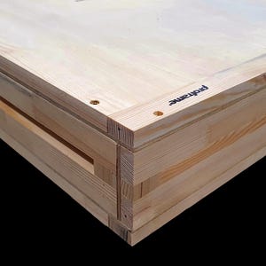Può includere: Primo piano di una cornice in legno con la scritta "proframe" stampata sul lato. La cornice è realizzata in legno chiaro e ha una costruzione a strati. L'angolo della cornice è visibile, mostrando l'incastro.