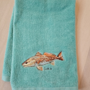 May include: A teal bath towel with an embroidered redfish design and the word "Castro" embroidered below the fish.