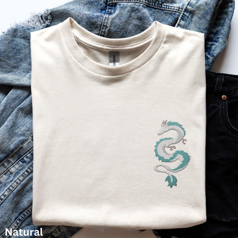 Puede incluir: Una camiseta de color crema con un gr&aacute;fico de drag&oacute;n verde y blanco en el lado izquierdo del pecho.