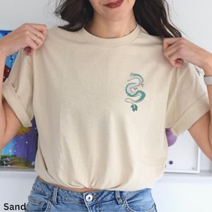 Puede incluir: Una camiseta de color arena con un peque&ntilde;o dise&ntilde;o de drag&oacute;n verde bordado en la parte delantera.