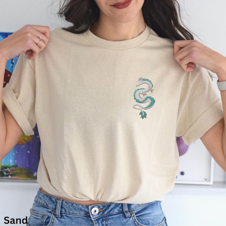 Puede incluir: Una camiseta de color arena con un peque&ntilde;o dise&ntilde;o de drag&oacute;n verde bordado en la parte delantera.