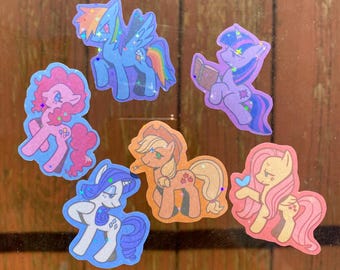 May include: A collection of seven colorful pony stickers. Each sticker features a different pony character with unique designs and colors, including pink, blue, purple, and orange. The stickers have a holographic, glittery finish.