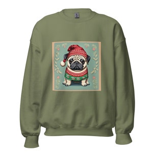 Op de afbeelding: Een groen sweatshirt met een feestelijke mops die een rood-witte kerstmanmuts en een groen-rode trui draagt. De mops is omringd door een krans van hulst en bessen.