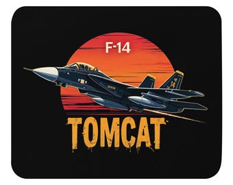 May include: A black mouse mat with a stylized illustration of an F-14 Tomcat fighter jet in flight against a red and orange sunset. The text "F-14" is above the jet, and "TOMCAT" is below. The mouse mat has rounded corners.