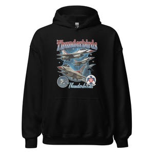 May include: Black hooded sweatshirt featuring a graphic of the Thunderbirds, a U.S. Air Force demonstration squadron. The design includes images of jets in flight, the squadron's name, and emblems in red, white, and blue.