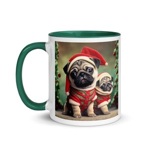 Op de afbeelding: Witte keramische mok met een groene rand. De mok heeft een feestelijk beeld van twee mopshonden die kerstmanmutsen en rode en gouden kerstoutfits dragen. De mopshonden zitten voor een groene kerstboom met rode kerstballen.