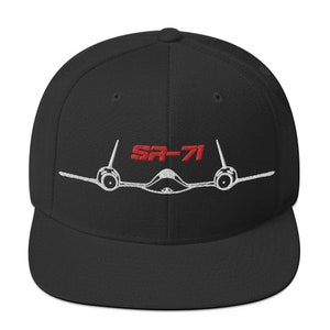 以下が含まれることがあります： 黒色のフィットしたベースボールキャップに、白黒の刺繍でSR-71ブラックバード機のデザインが施されています。