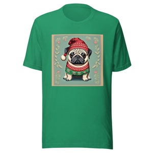 Op de afbeelding: Een groen T-shirt met een vintage-achtige illustratie van een mops die een rood-witte kerstmanmuts en een groen-witte kersttrui draagt. De mops staat op een lichtblauwe achtergrond met witte sneeuwvlokken en rode bessen.