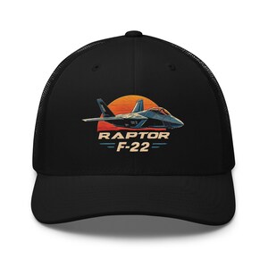 Peut inclure: Casquette de camionneur noire en mesh avec un graphique vintage d'un avion de chasse F-22 Raptor sur fond de coucher de soleil. Le texte "RAPTOR F-22" est imprimé sous l'avion.