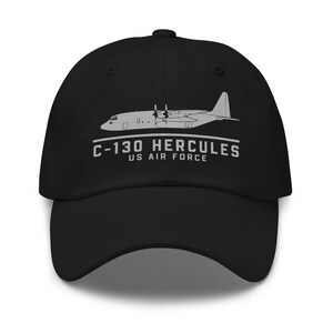 Może przedstawiać: Czarna czapka bejsbolowa z białym nadrukiem samolotu C-130 Hercules. Pod spodem znajduje się napis "C-130 HERCULES US AIR FORCE". Czapka ma zakrzywiony daszek i strukturalny krój.