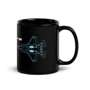 May include: Black ceramic mug featuring a light blue schematic of an F-35 fighter jet. The text "F-35" is printed on the side of the mug. The mug has a glossy finish and a curved handle.
