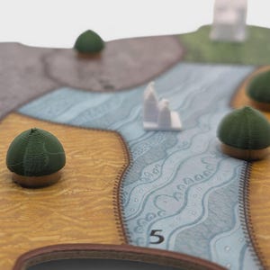 May include: A close-up of a board game with a map design. The game board features tan, green, and blue sections with small, green, dome-shaped game pieces. There are also small, white, architectural game pieces.
