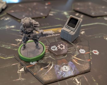 May include: A board game scene with a miniature grey figure on a green base, a grey control panel, and game tokens. The game board is dark with hexagonal spaces and numbered markers. The scene suggests a strategy or sci-fi themed game.