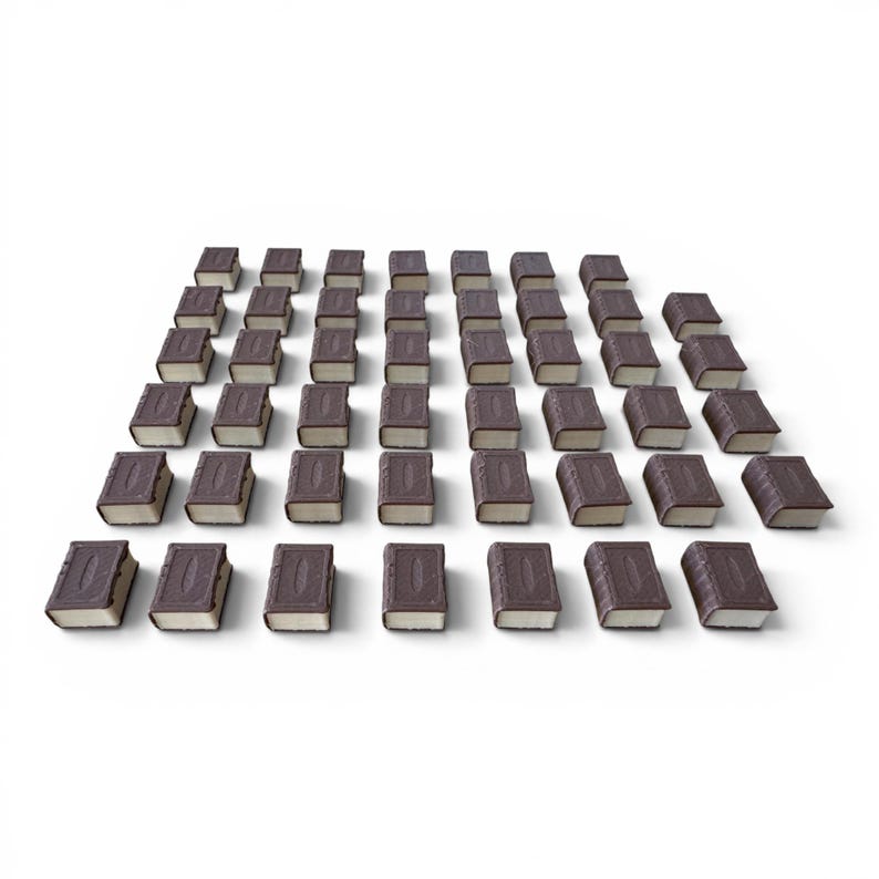 May include: A collection of miniature book-shaped objects arranged in a grid pattern. Each book has a dark brown cover with embossed details and a light-colored page section. The objects are set against a plain white background.