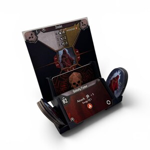 Könnte beinhalten: Ein schwarzer Spielkartenhalter aus Kunststoff mit einer hohen Charakterkarte mit der Aufschrift Zealot und Totenkopf-Symbolen sowie kleineren Karten, darunter eine mit der Aufschrift Unholy Flame und Angriffsstatistiken.