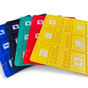 Peut inclure: Une pile de plateaux de jeu en plastique colorés en bleu, noir, vert, rouge et jaune. Chaque plateau présente une grille de petits carrés et diverses formes géométriques et symboles. Les plateaux sont empilés en biais.
