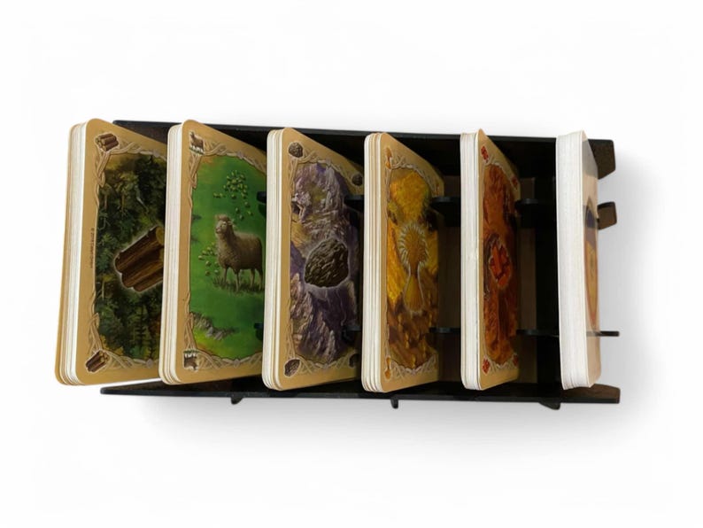 Puede incluir: Un soporte de tarjetas de madera negro con seis ranuras, cada una con una tarjeta diferente con una ilustraci&oacute;n de tem&aacute;tica natural. Las tarjetas tienen un borde dorado y est&aacute;n dispuestas en fila.