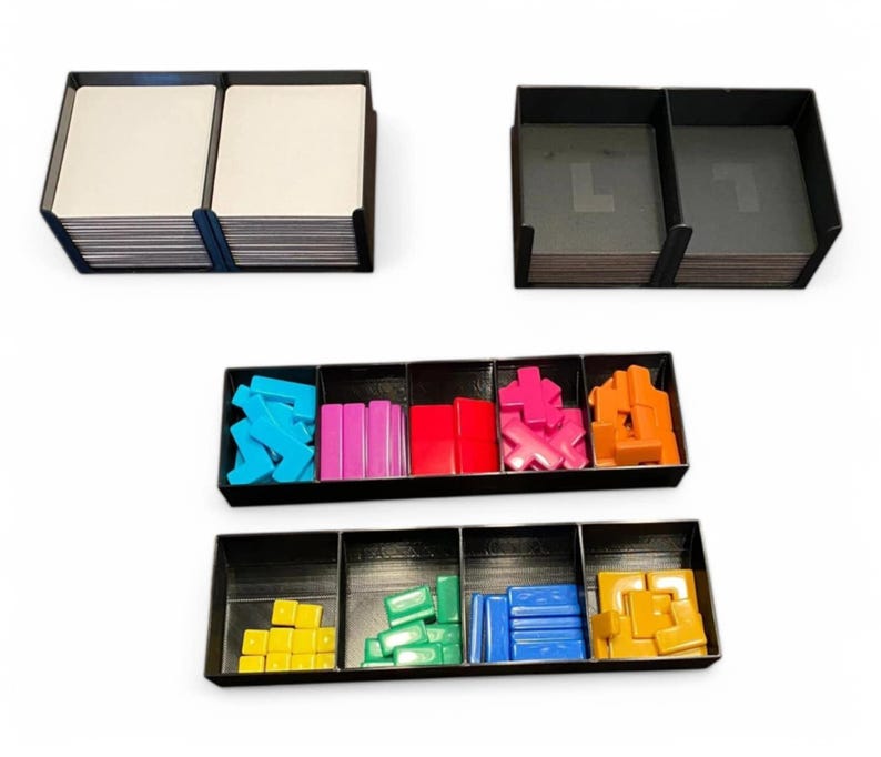May include: Black game organisers with various coloured game pieces and cards. The organisers are divided into compartments, holding blue, pink, red, orange, yellow, and green game components. The cards are stacked in two separate organisers.