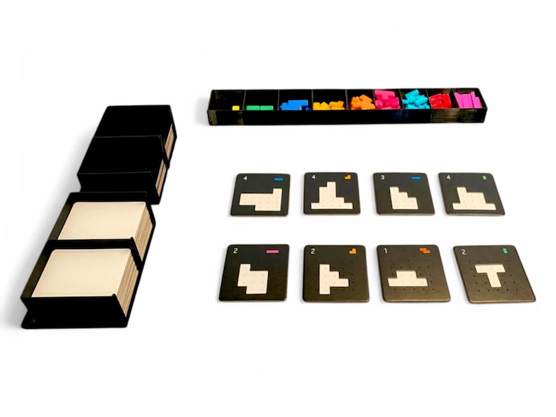 May include: A board game set with black components and colourful pieces. The set includes a stack of black boxes with white cards, a tray with coloured blocks, and several square cards with geometric shapes and numbers.