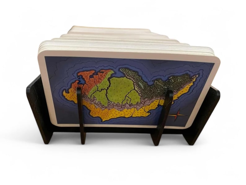 Puede incluir: Un soporte de tarjetas negro con un mapa de una isla ficticia en la tarjeta superior. El mapa es colorido con secciones verdes, amarillas, naranjas y rojas. El soporte de tarjetas est&aacute; hecho de madera y tiene tres patas.