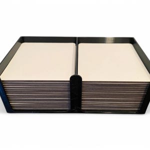 May include: A black card holder, rectangular in shape, divided into two sections, each containing a stack of white cards. The design is simple and modern, ideal for organising cards.