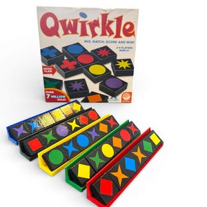 Puede incluir: Se muestra el juego de mesa "Qwirkle" con el lema "Mix, Match, Score and Win!". El juego presenta fichas de madera con diferentes formas y colores, y soportes para fichas en azul, amarillo, verde y rojo. El juego es para 3-4 jugadores.