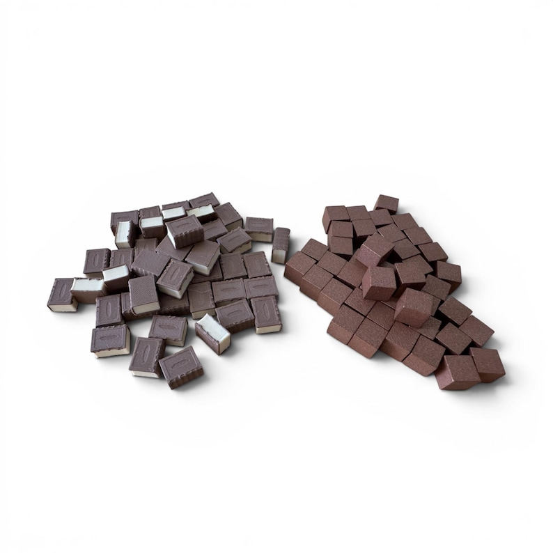 May include: Two piles of small, dark brown, rectangular objects. One pile has a white layer on one side, resembling miniature books. The other pile consists of solid brown blocks. The objects are arranged on a white background.