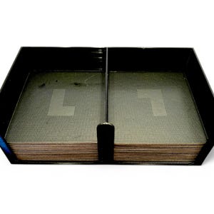 May include: Black rectangular desk organiser with two compartments. Each compartment contains a stack of brown coasters with a perforated surface. A black divider separates the compartments.
