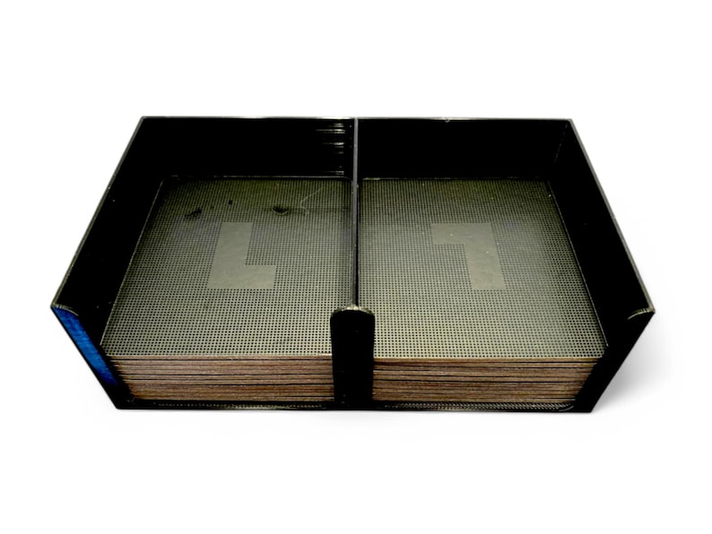 May include: Black rectangular desk organiser with two compartments. Each compartment contains a stack of brown coasters with a perforated surface. A black divider separates the compartments.