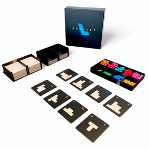 May include: A board game set with a black box labelled "PROJECT" in white and blue. The set includes black card holders, game cards, and colourful plastic game pieces. The cards have white geometric shapes.