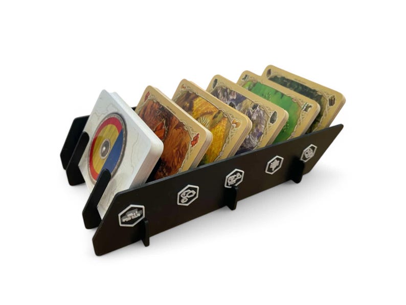 Puede incluir: Un soporte de tarjetas de madera negro con cinco ranuras para guardar tarjetas. El soporte tiene un dise&ntilde;o hexagonal y est&aacute; decorado con detalles met&aacute;licos plateados. Las tarjetas son de diferentes colores y tienen varios dise&ntilde;os.