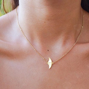 Puede incluir: Un collar de cadena dorada con un pequeño colgante delicado en forma de manta raya.