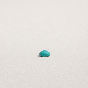 May include: A single, small, polished turquoise gemstone with a smooth, rounded, dome-like shape. The stone displays a vibrant cyan-blue color with subtle, darker natural veining patterns distributed across its polished, reflective surface.
