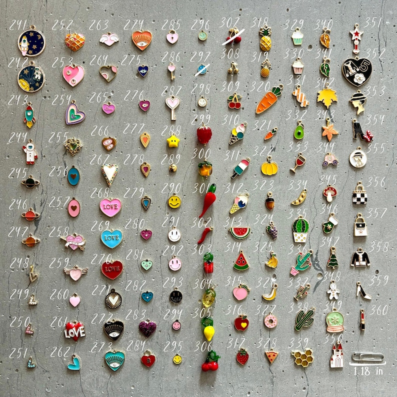 K&ouml;nnte beinhalten: Eine Sammlung von 100 Emaille-Anh&auml;ngern in verschiedenen Farben und Designs. Die Anh&auml;nger sind in Reihen auf einer grauen Oberfl&auml;che angeordnet. Die Anh&auml;nger umfassen Herzen, Sterne, Ananas, Eiswaffeln und mehr.