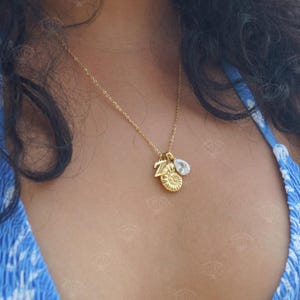 Op de afbeelding: Een gouden ketting met een traanvormige kristallen hanger, een letterhanger en een schelp hanger.