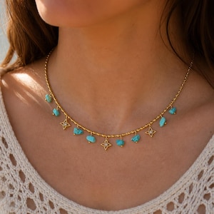 Puede incluir: Un collar de cadena en tono dorado que presenta dijes alternados de pequeñas piedras irregulares de color turquesa y colgantes en forma de estrella con una piedra clara central. La cadena tiene un diseño delicado con pequeñas cuentas.