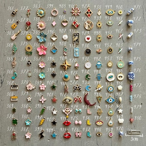 K&ouml;nnte beinhalten: Eine Sammlung von 100 kleinen Charms, jeder mit einem anderen Design. Die Charms sind aus Metall und haben eine Vielzahl von Farben, darunter Gold, Silber, Blau, Rot, Gr&uuml;n und Pink. Die Charms sind in einem Rastermuster auf einer grauen Oberfl&auml;che angeordnet. Die Charms sind von 361 bis 480 nummeriert.