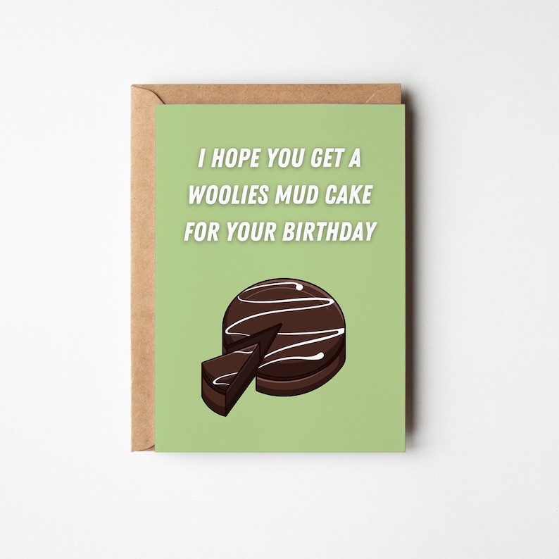 May include: A birthday card with a green background and a brown envelope. The card reads "I HOPE YOU GET A WOOLIES MUD CAKE FOR YOUR BIRTHDAY" above a chocolate mud cake illustration with a missing slice. The card is rectangular.